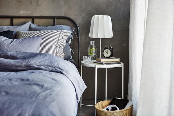 Opredt seng med et sengebord, et glas vand, bøger, et vækkeur og en lampe med lysdæmper.