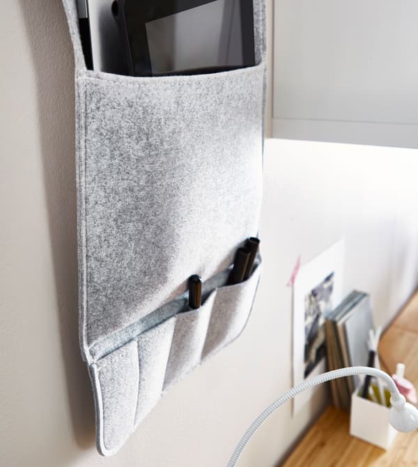 Organiseur mural gris en tissu, accroché au mur au-dessus d’un bureau.