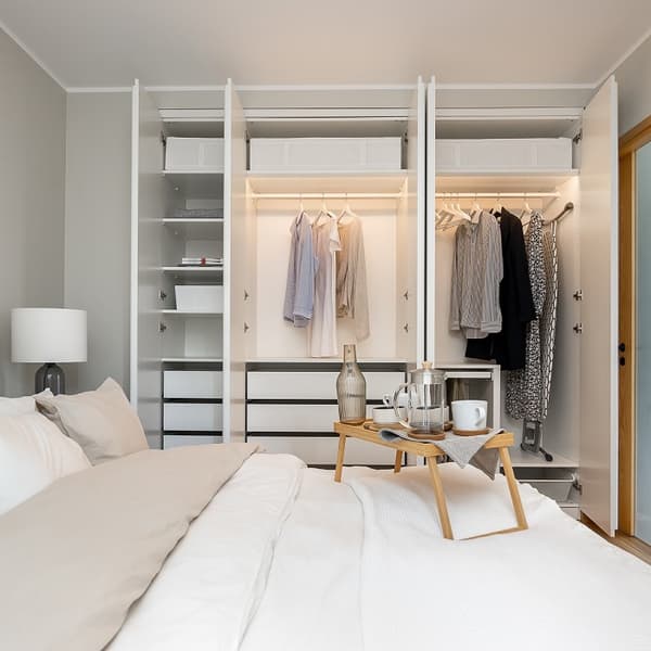 Organized white wardrobe with hanging clothes and breakfast tray on bed