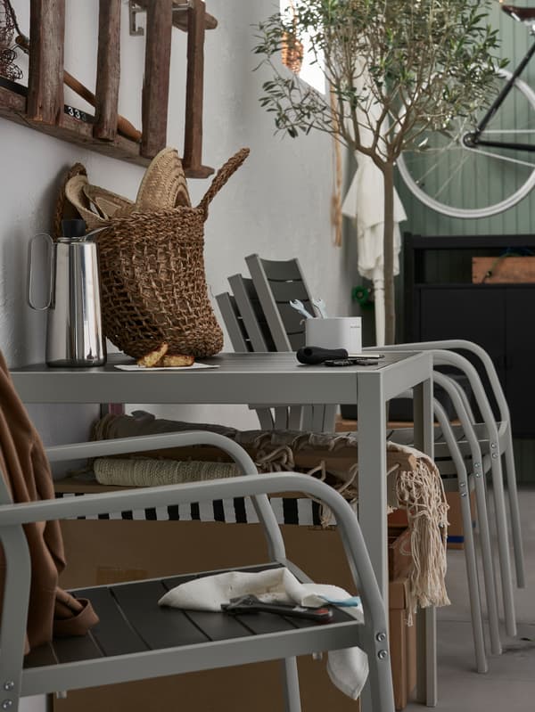 Outdoor chairs, one single and others stacked by a wall, with an outdoor table holding a coffee pot, a bag and tools.