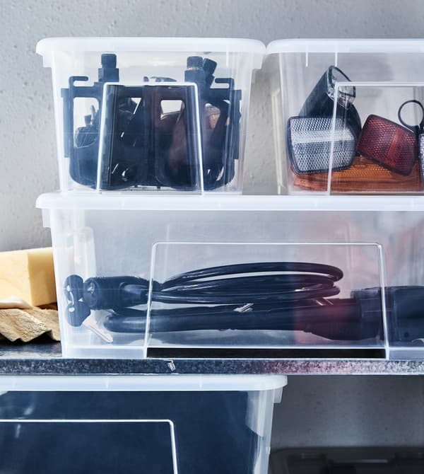 Outdoor gear and sports accessories are stored in clear plastic boxes on a shelf.