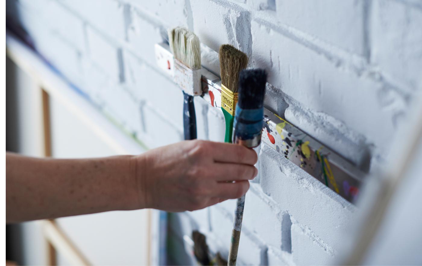 Paintbrushes are being mounted to a magnetic knife rack on the wall.