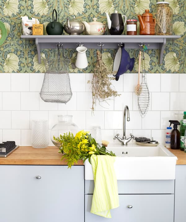 Pale grey kitchen cupboards, wooden worktops and a white sink, with white tiles and a grey shelf above.