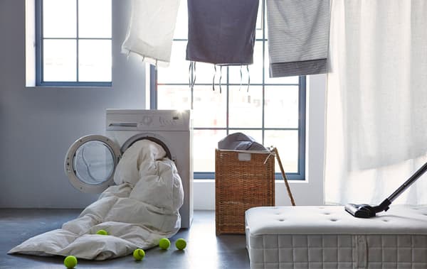 Panier à linge ouvert, matelas avec un aspirateur dessus et sèche-linge avec une couette dans le tambour