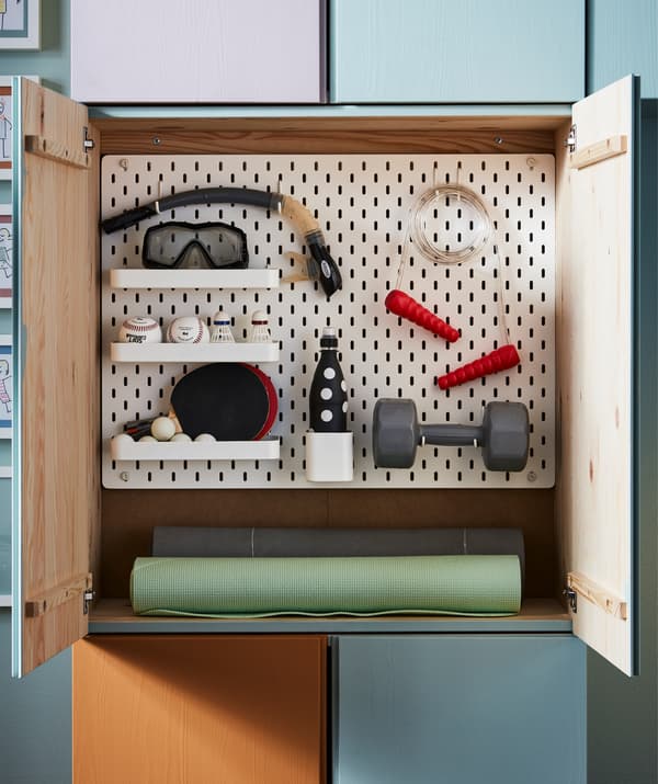 Panneau perforé SKÅDIS blanc placé à l’intérieur d’un rangement IVAR accueillant plusieurs articles de sport.