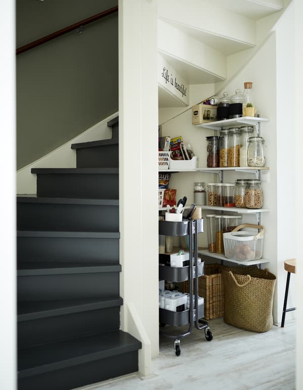 Pantry shelves and a trolley in an alcove under the stairs.