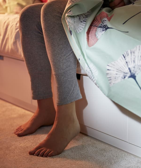 Partie inférieure d'un lit avec boîtes de rangement intégrées. Deux pieds se posent sur un tapis moelleux.