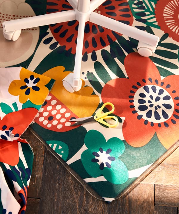 Partie inférieure d'une chaise pivotante enfant sur une protection de sol posée sur un tissu à motif floral.
