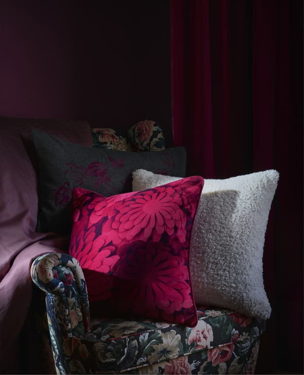 Patterned cushions on a dark floral armchair against a dark red backdrop.