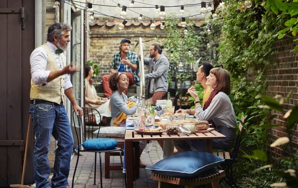People sitting around a wooden table in a backyard area with brick walls and plants.