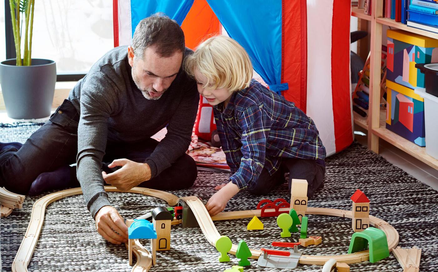 Père et enfant jouant avec la locomotive LILLABO à la maison, avec une tente de jeu rayée en arrière-plan.
