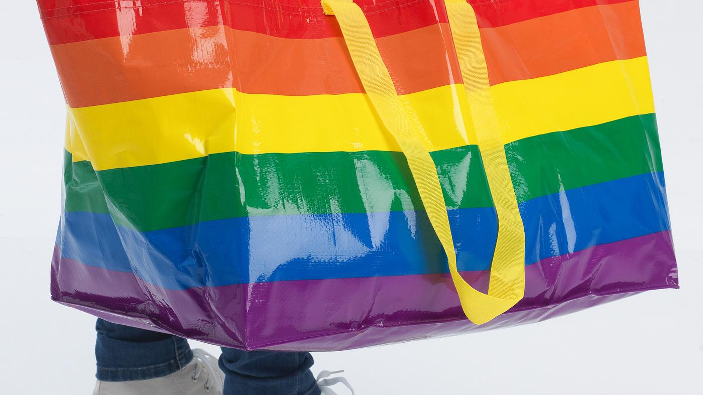Person carrying a rainbow-coloured STORSTOMMA carrier bag.
