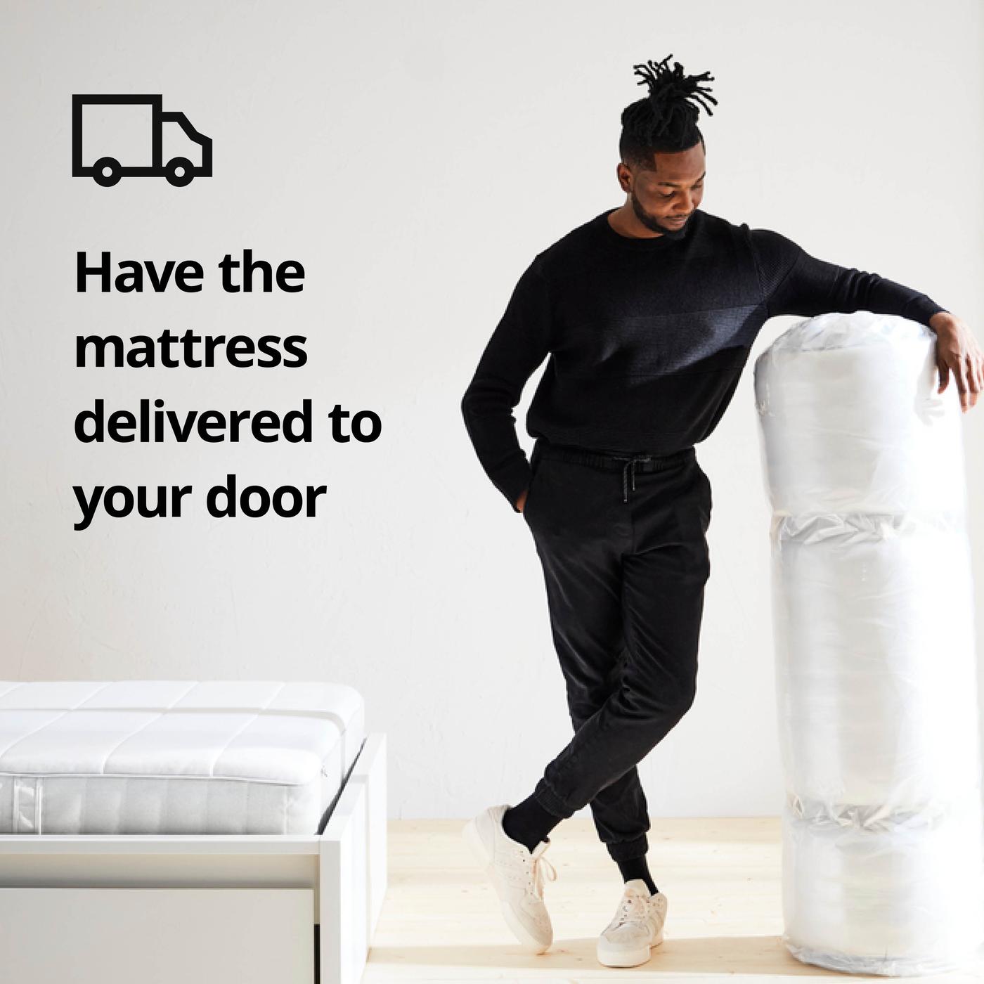 Person leaning against rolled up mattress in white room; on the left a bed with mattress and on the image the text "Have the mattress delivered to your door" with truck icon.