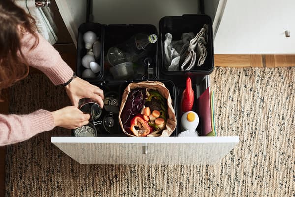 Person placing an empty can into a VARIERA waste sorting system with multiple bins.
