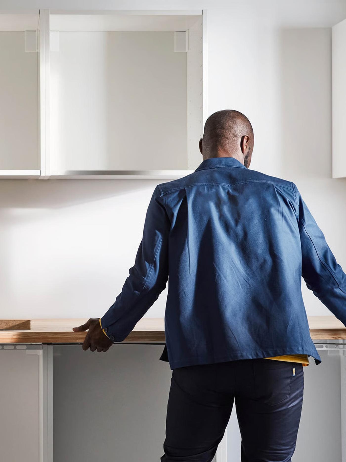 Person standing at a kitchen counter with empty cabinets on the wall.
