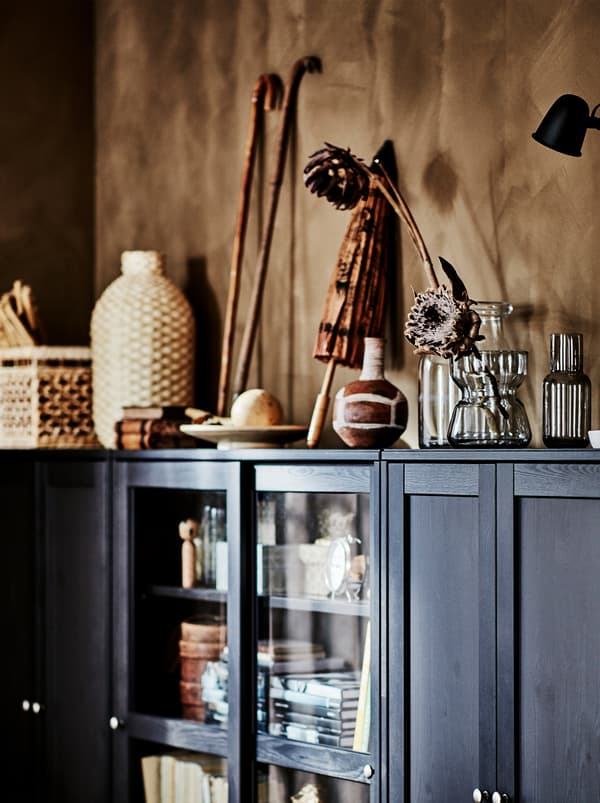 Personal items from travels, things in natural materials, and glass vases with flowers on top of a dark brown HAVSTA cabinet.