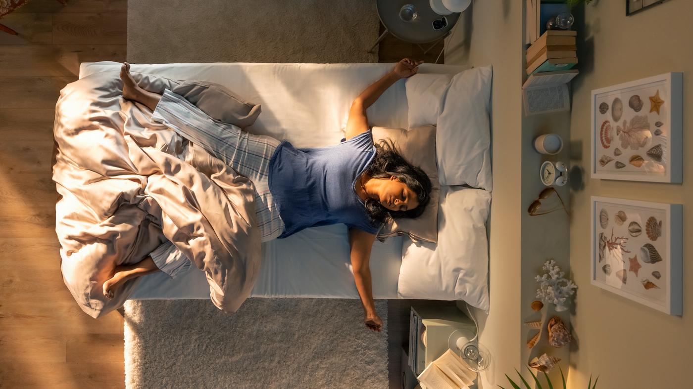 Personne au lit, allongée sur le dos et en partie couverte d’une housse de couette KRITSUGA beige. Sa tête repose sur une taie d’oreiller de la même série.