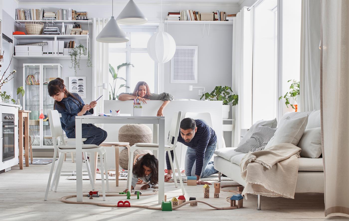 Petit intérieur où une famille joue avec un train LILLABO installé dans une pièce avec un lit, un canapé, une table, une kitchenette et des rangements.