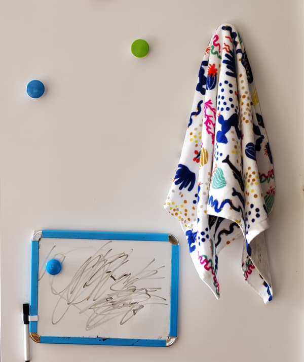 Petit tableau blanc avec feutre et objets à motifs pendus à des crochets colorés.