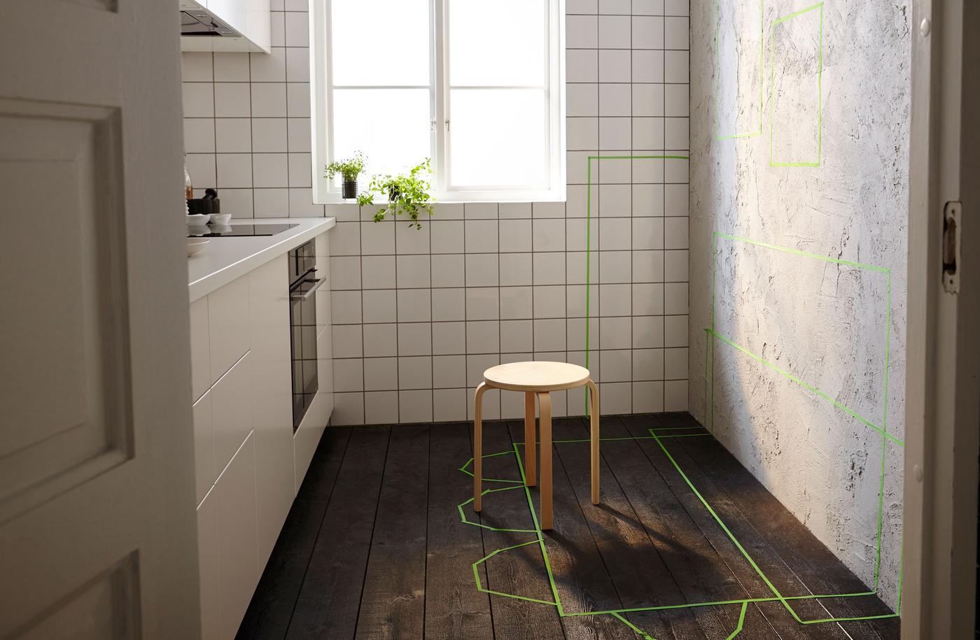 Petite cuisine avec mur libre d’un côté, marquages à l’adhésif vert à l’emplacement des futurs rangements, tables et chaises. 