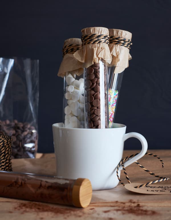 Petites fioles en verre remplies de garnitures pour chocolats chauds, placées dans un mug blanc.