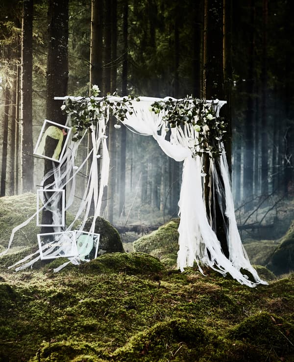Photomaton réalisé avec des bandelettes découpées dans des voilages et des fleurs artificielles attachées à une barre suspendue à l’horizontale, pour une fête de noces dans la forêt