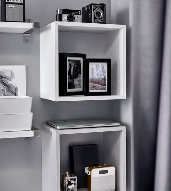 Photos, cameras, and a stereo are displayed on a shelf above a bed.