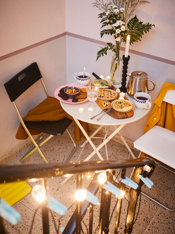 Pianerottolo con alcune sedie pieghevoli GUNDE, un tavolino con qualche snack, un tagliere FASCINERA, fiori e caffè - IKEA