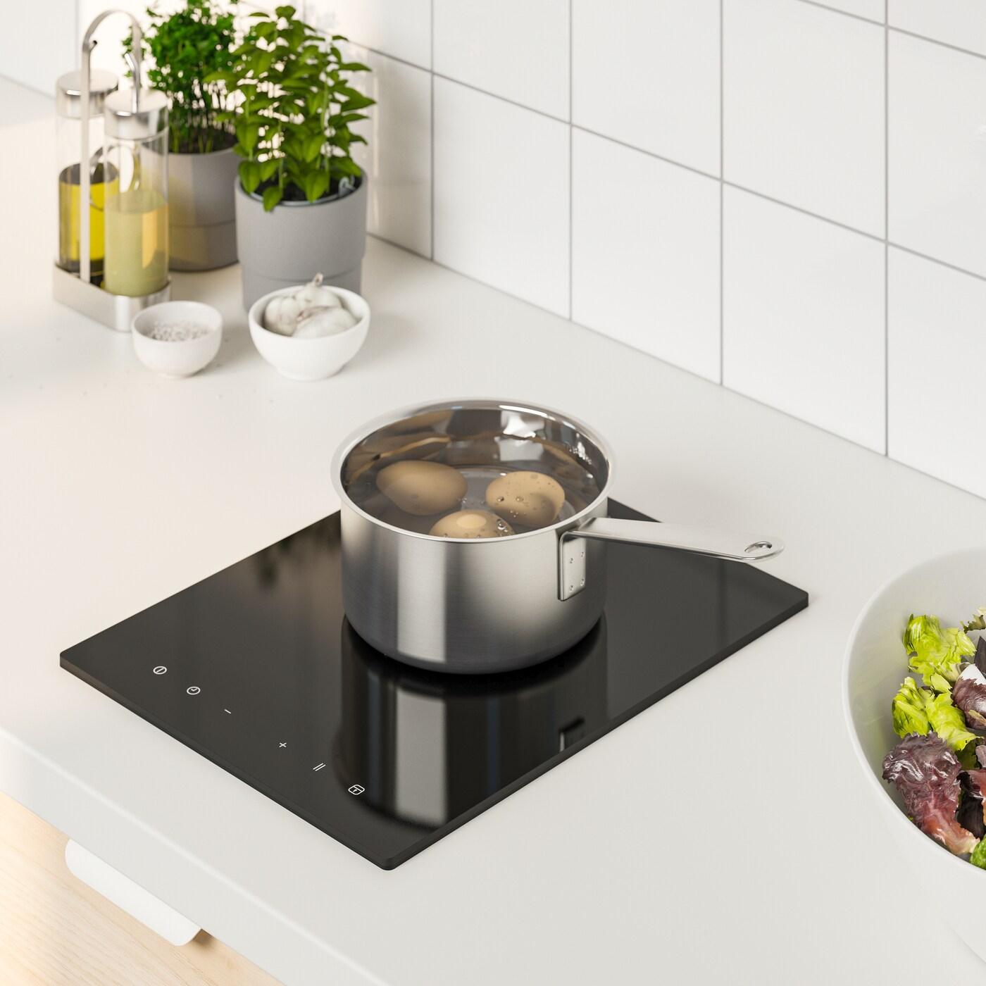Piano cottura a induzione LAGAN nero, con una pentola di patate e due piante in portavasi - IKEA.
