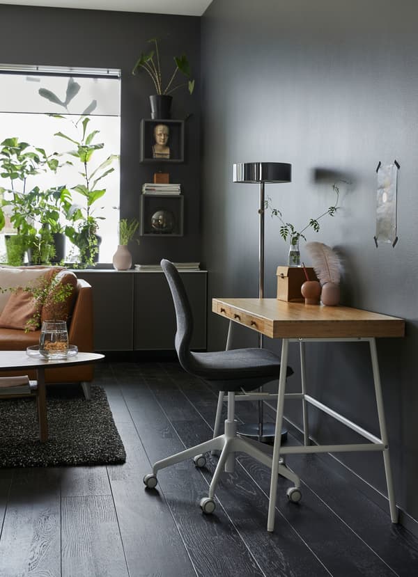 Piccola scrivania con piano in bambù e gambe bianche in un soggiorno con pareti color grigio scuro – IKEA