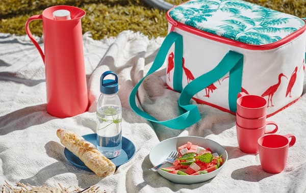 Picnic with a white throw on grass, set with a SOMMARLIV cooling bag, TALRIKA mugs and a summer salad in a TALRIKA plate.