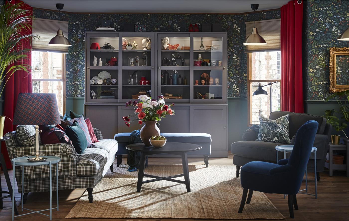 Picture of a living room with sofas, chairs, side tables, floral walls and a large glass-fronted cabinet.