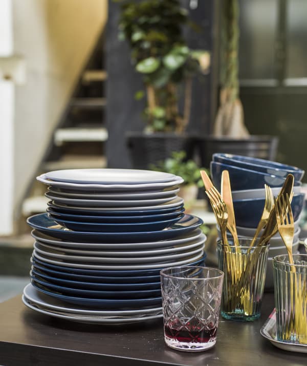 Pile d’assiettes blanches et bleues, et couverts dorés déposés sur une table