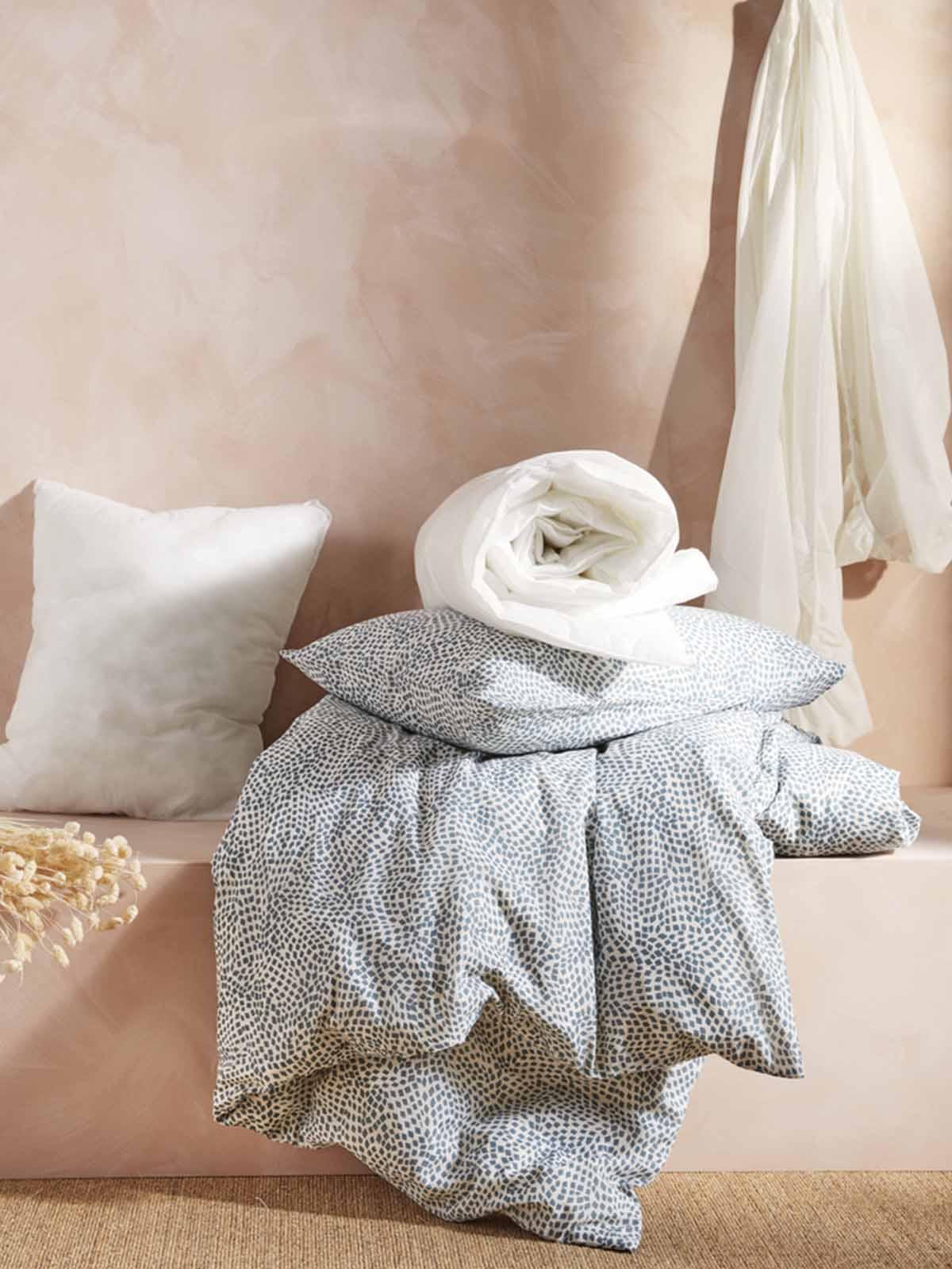 Pillows and cushions in various colours are stacked on top of one another on a bed.