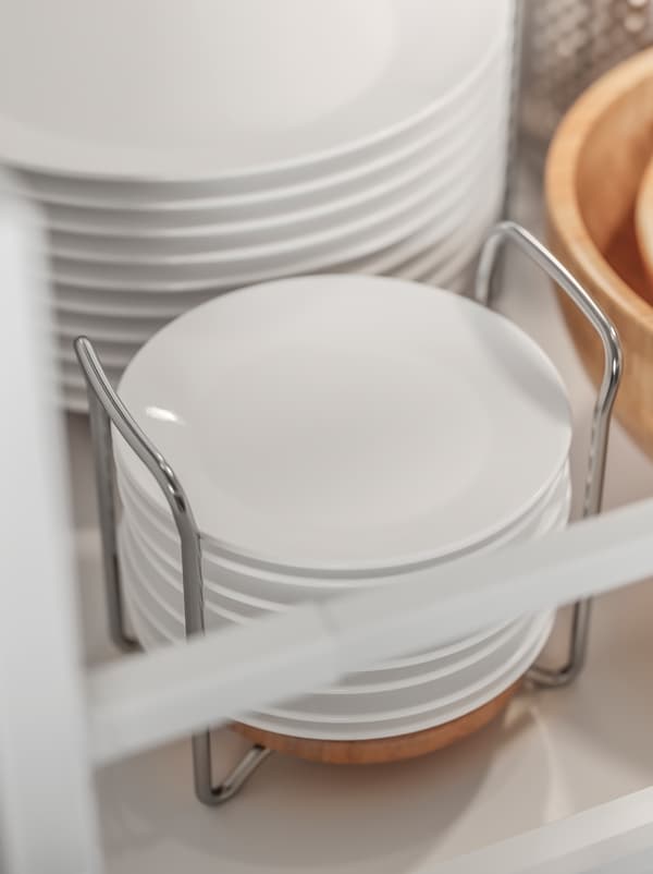 Pinggan berwarna putih bertindan dan diletakkan dalam bekas pinggan VARIERA yang dibuat daripada keluli tahan karat dan kayu.