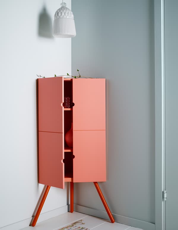 Pink wooden IKEA corner cabinet with a white glass lampshade hanging above it.