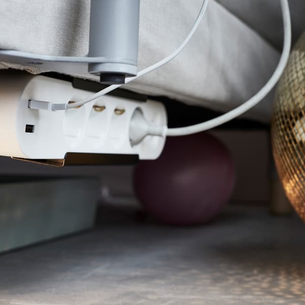 Placez un bloc multiprise IKEA KOPPLA sous le canapé pour pouvoir recharger facilement vos appareils tout en les gardant à portée de main.