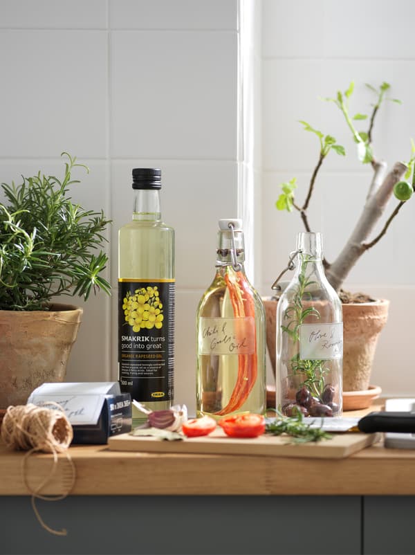 Plan de travail de cuisine avec des cache-pots et deux bouteilles en verre KORKEN contenant de l’huile de colza parfumée aux épices et aux herbes aromatiques.