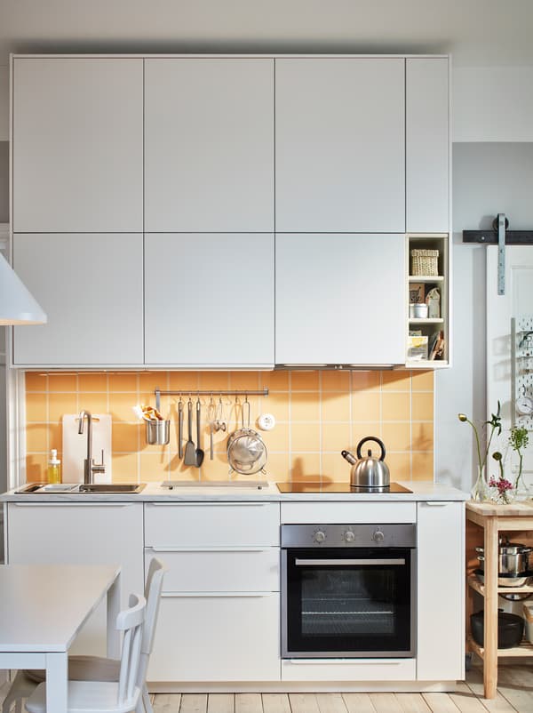 Plan de travail de cuisine avec évier, table de cuisson et ustensiles, encadré de rangées d’armoires dotées de façades METOD en blanc.