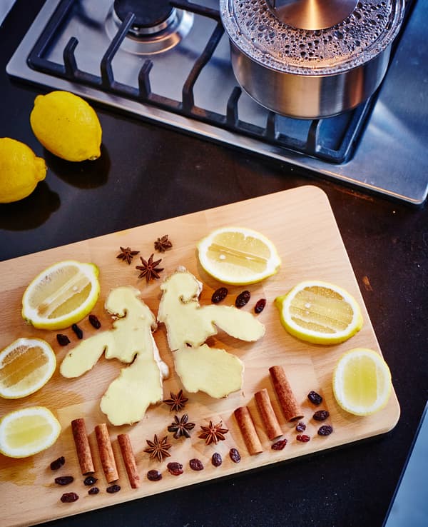 Planche à découper avec morceaux de citron, de cannelle, de gingembre, des clous de girofles et des raisins secs.