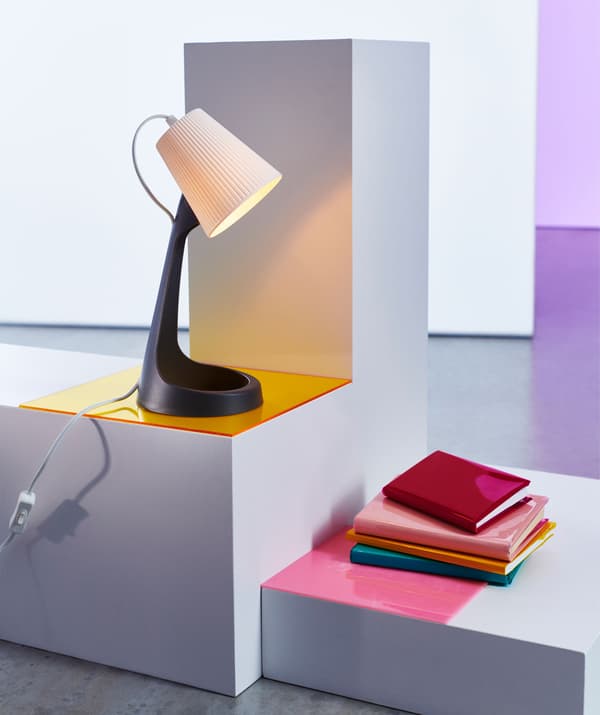 Plastová stolní lampa na podstavci, vedle je hromada knih