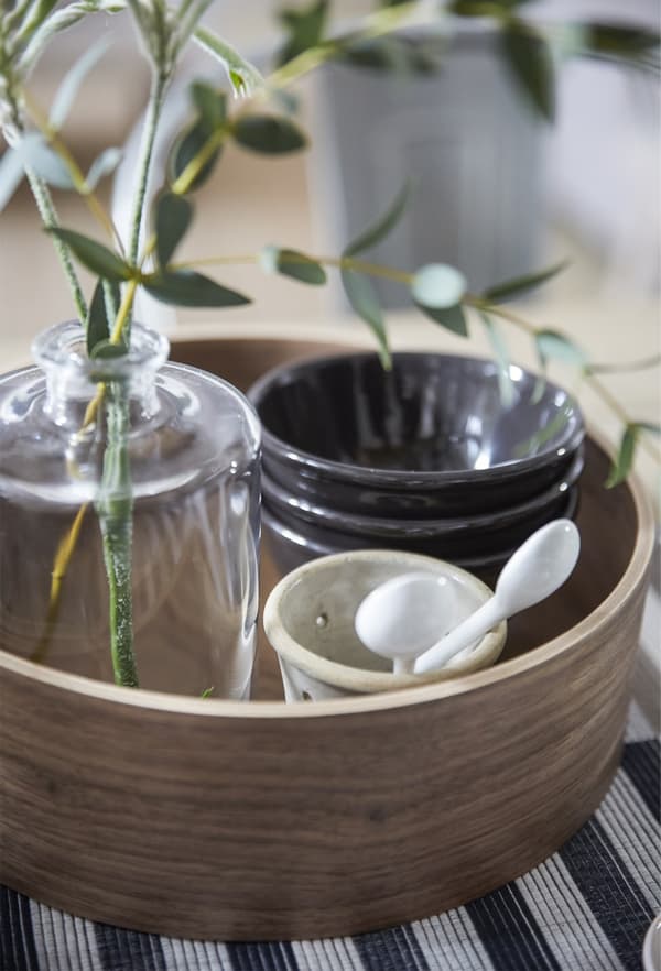 Plateau en bois rond contenant des bols et un vase avec des rameaux d’eucalyptus.