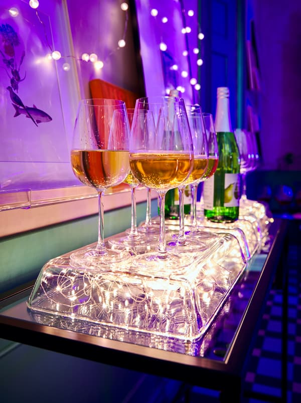 Plats à four MIXTUR renversés avec dessous des guirlandes lumineuses VISSVASS, formant un plateau lumineux pour des verres à vin remplis.