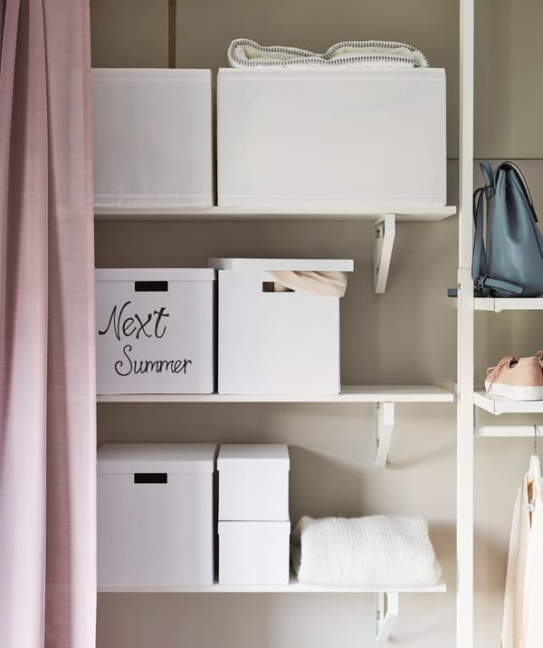 Plusieurs boîtes de rangement blanches sur des étagères de garde-robe.