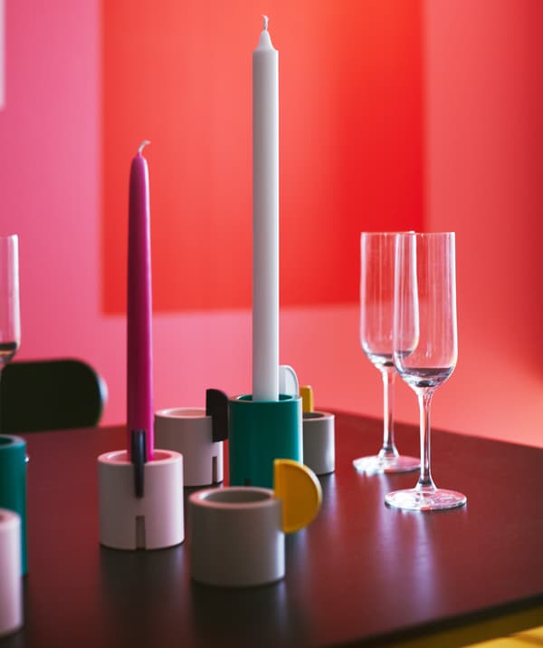 Plusieurs bougeoirs/photophores ÄDELHET en gris, blanc et vert ornés de bougies et posés sur une table.