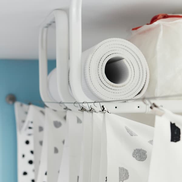 Plusieurs tringles à vêtements blanches MULIG fixées au plafond et utilisées comme rangement, cachées par un rideau tendu entre deux câbles pour rideau.