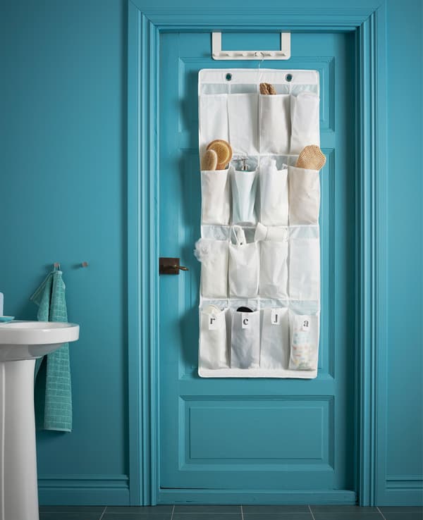 Porte de salle de bains avec organiseur pour chaussures dont les poches servent de rangement aux brosses, flacons, sprays et autres articles de toilette.