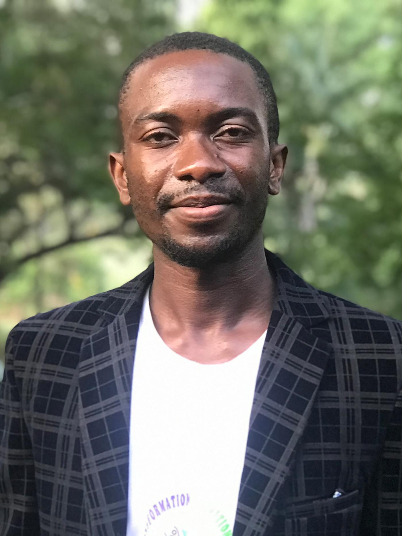 Portrait de Barthélémy, réfugié congolais tout sourire, vêtu d’une veste sombre sur un T-shirt blanc.