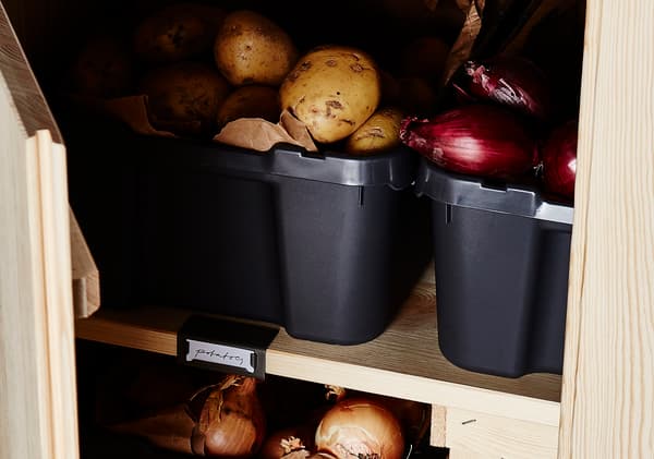 Potatoes and onions are stored in black plastic bins. 