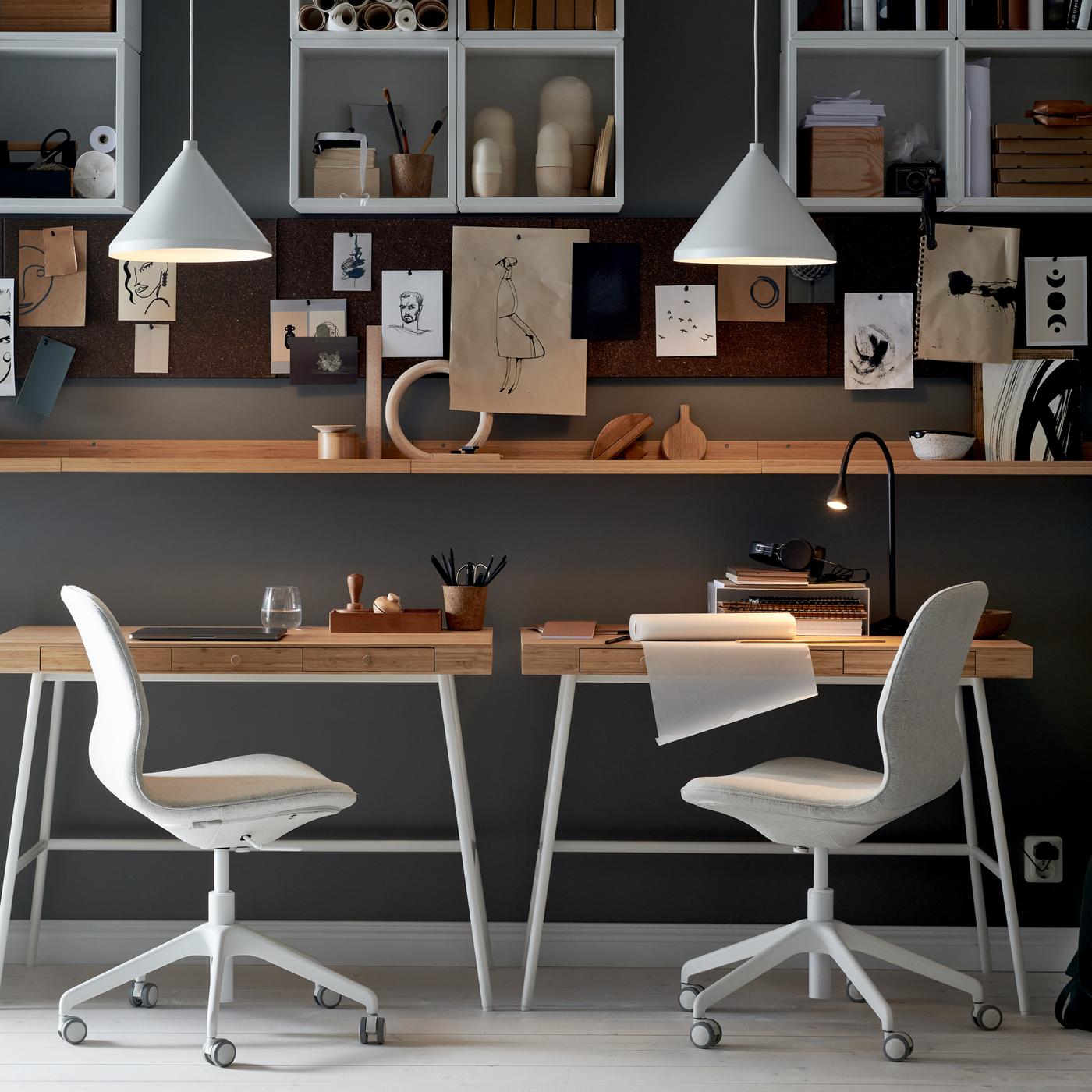 Pracovna se dvěma kancelářskými židlemi LÅNGFJÄLL u psacích stolů LILLÅSEN, s policemi, nástěnkami a bílými závěsnými lampami.